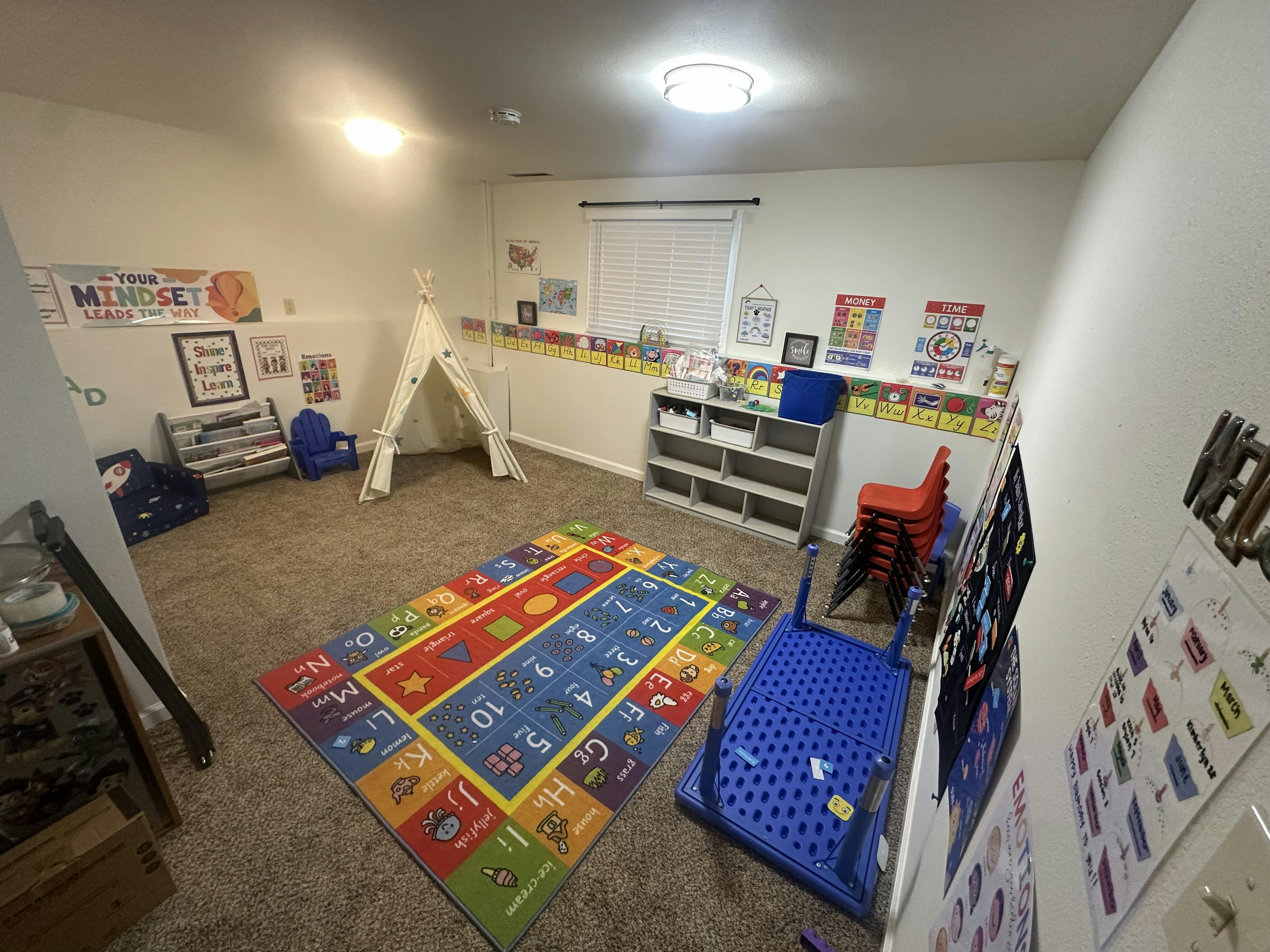 Classroom with an alphabet rug, tent, small chairs, and educational posters