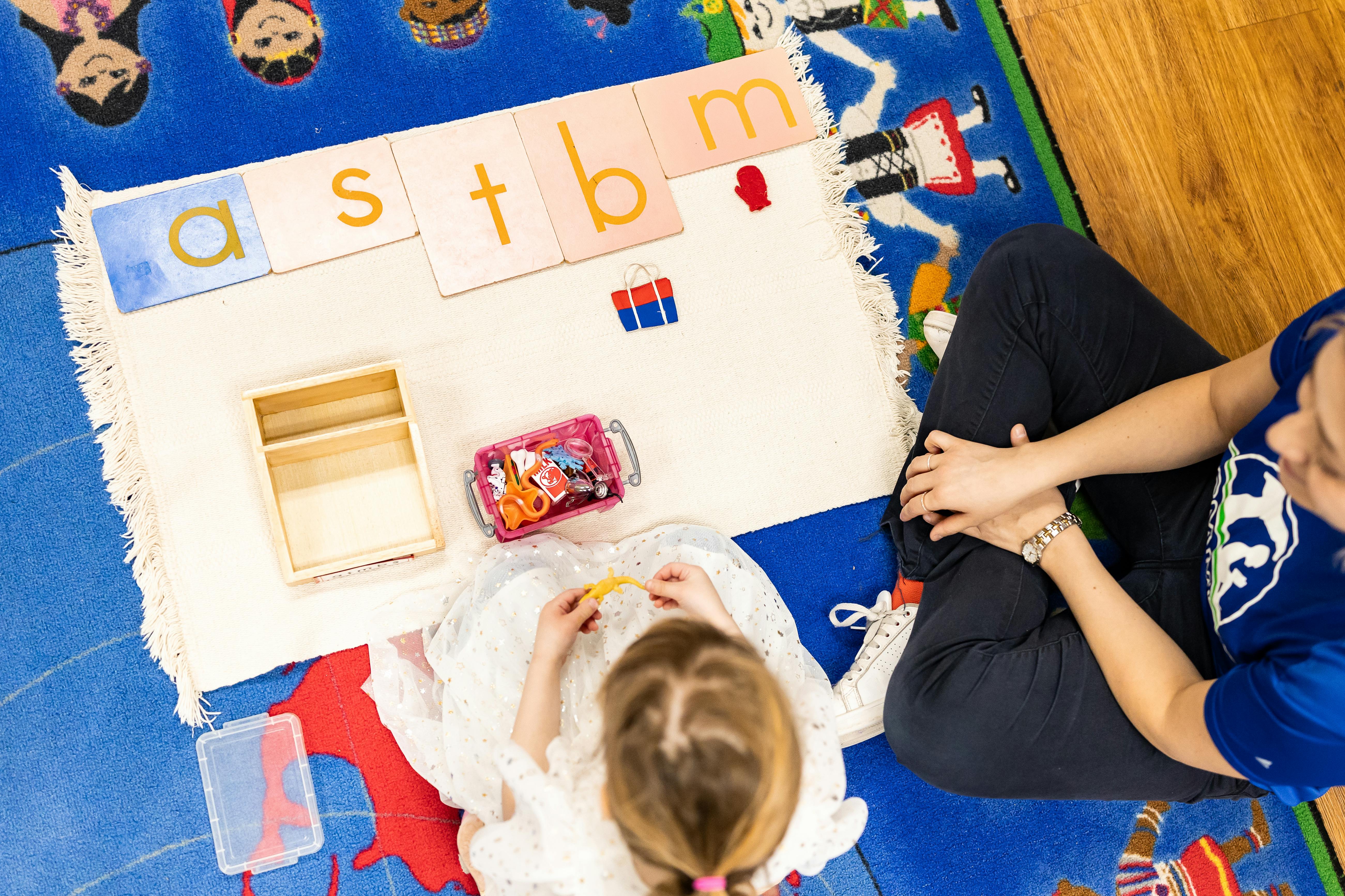 Child and person on a rug with alphabet cards and small toys