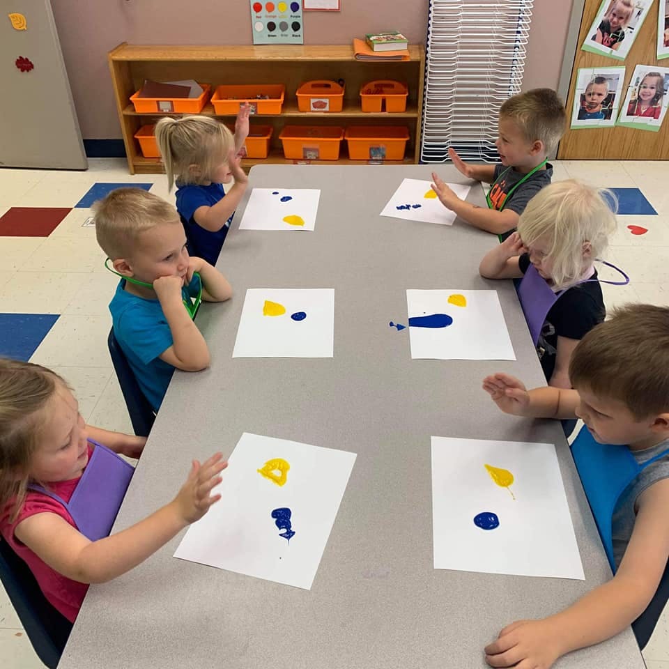 Children finger painting with yellow and blue paint on paper