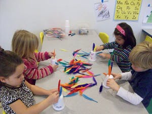 Four children making crafts with feathers at a table