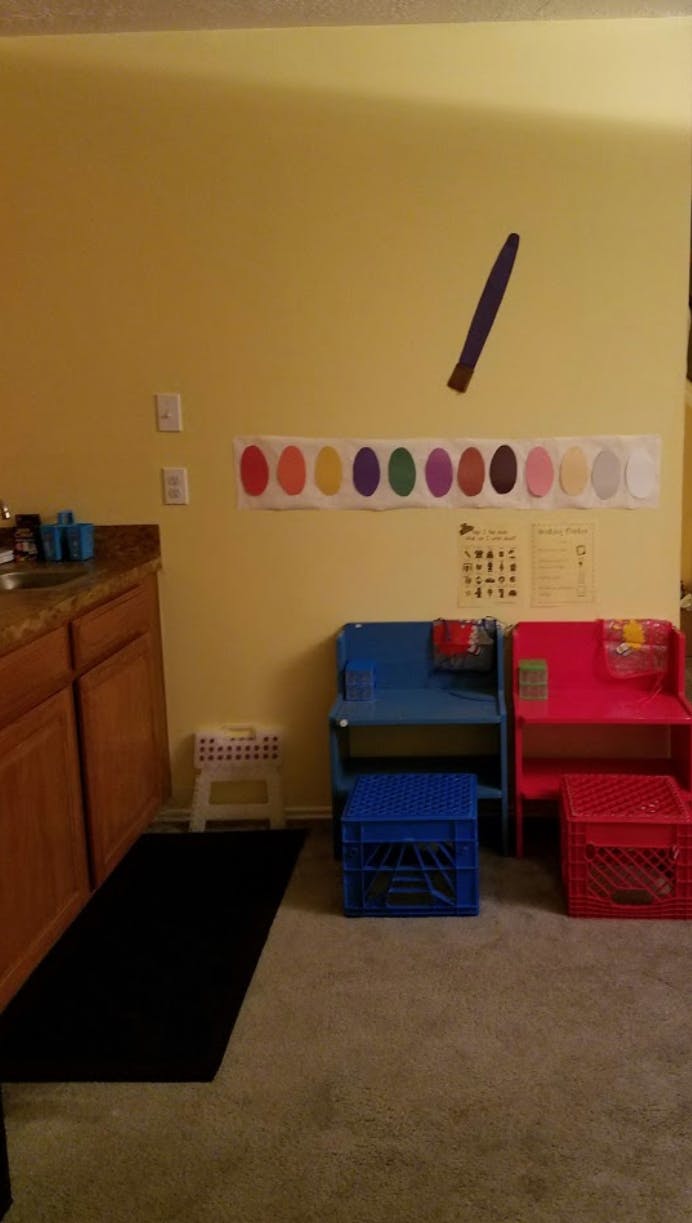 Classroom area with small chairs, crates, and color chart on wall