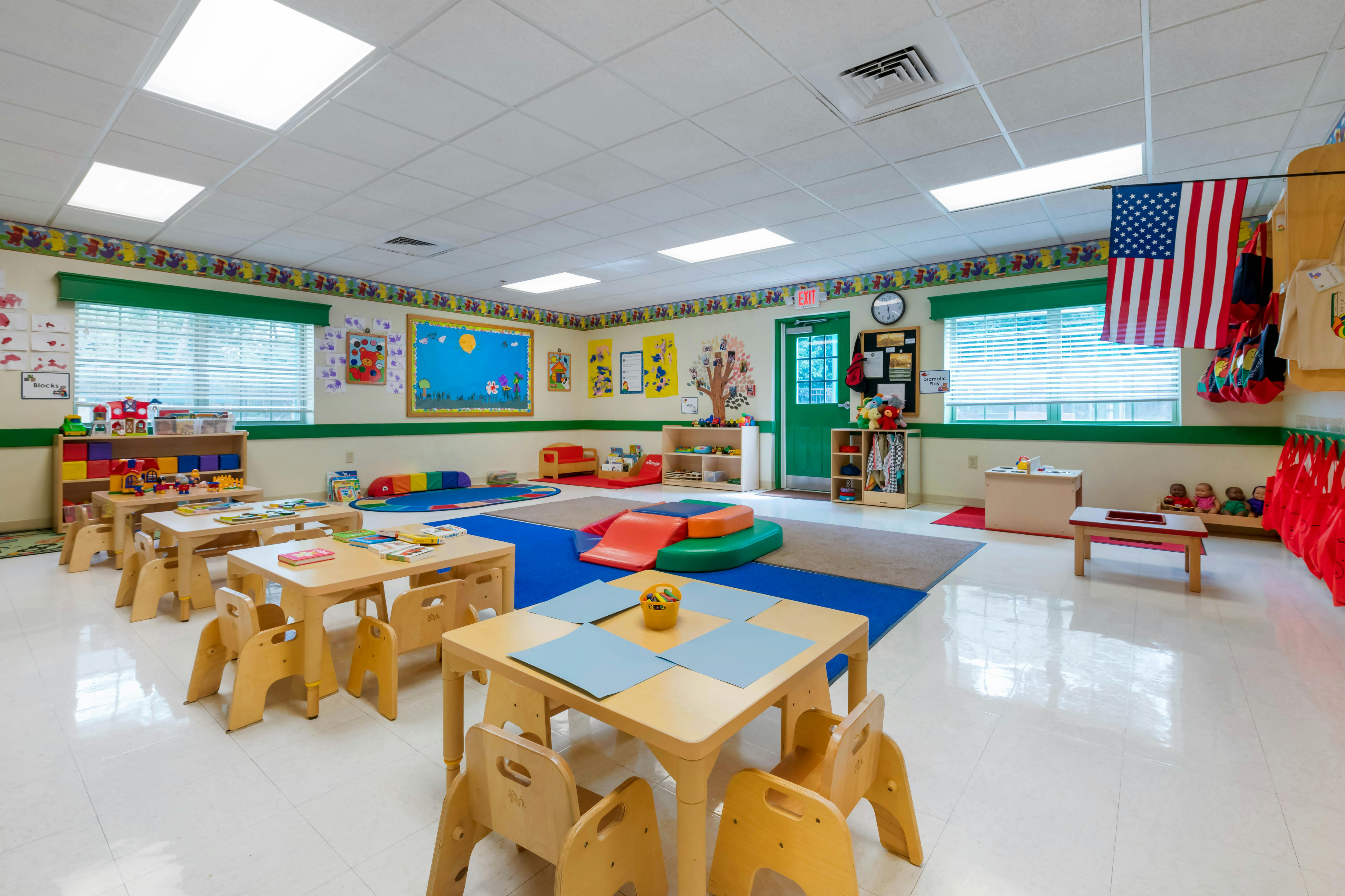 Classroom with small tables and chairs, colorful rugs, and play equipment