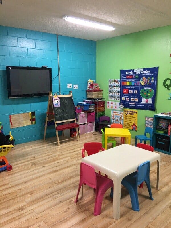 Classroom with small tables and chairs, a TV, and a chalkboard