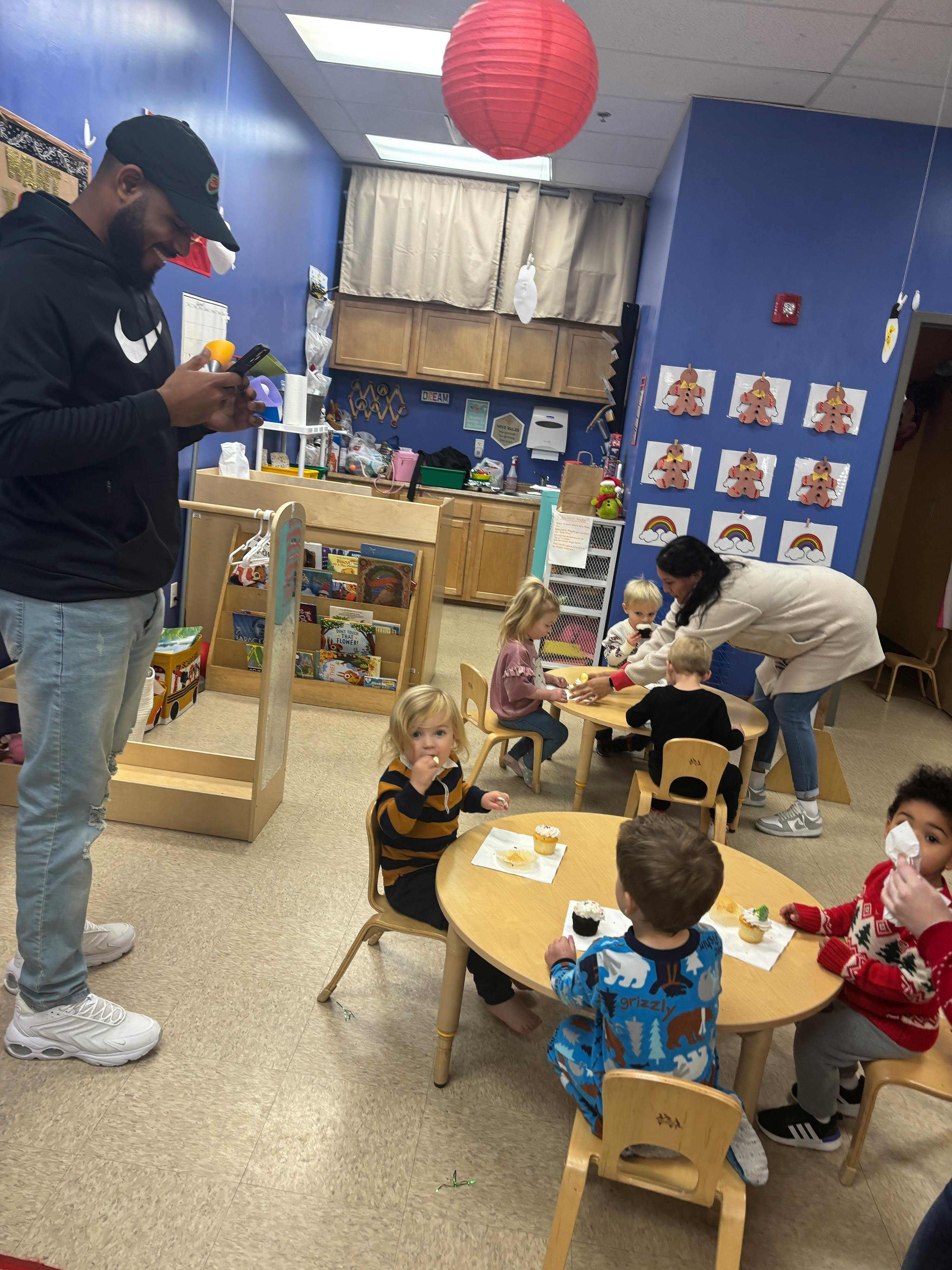 Person standing in a classroom with children seated at tables