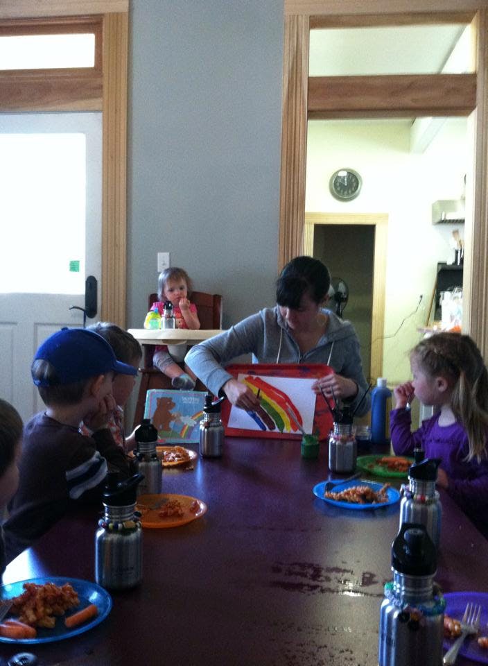Person showing children a rainbow drawing at a table