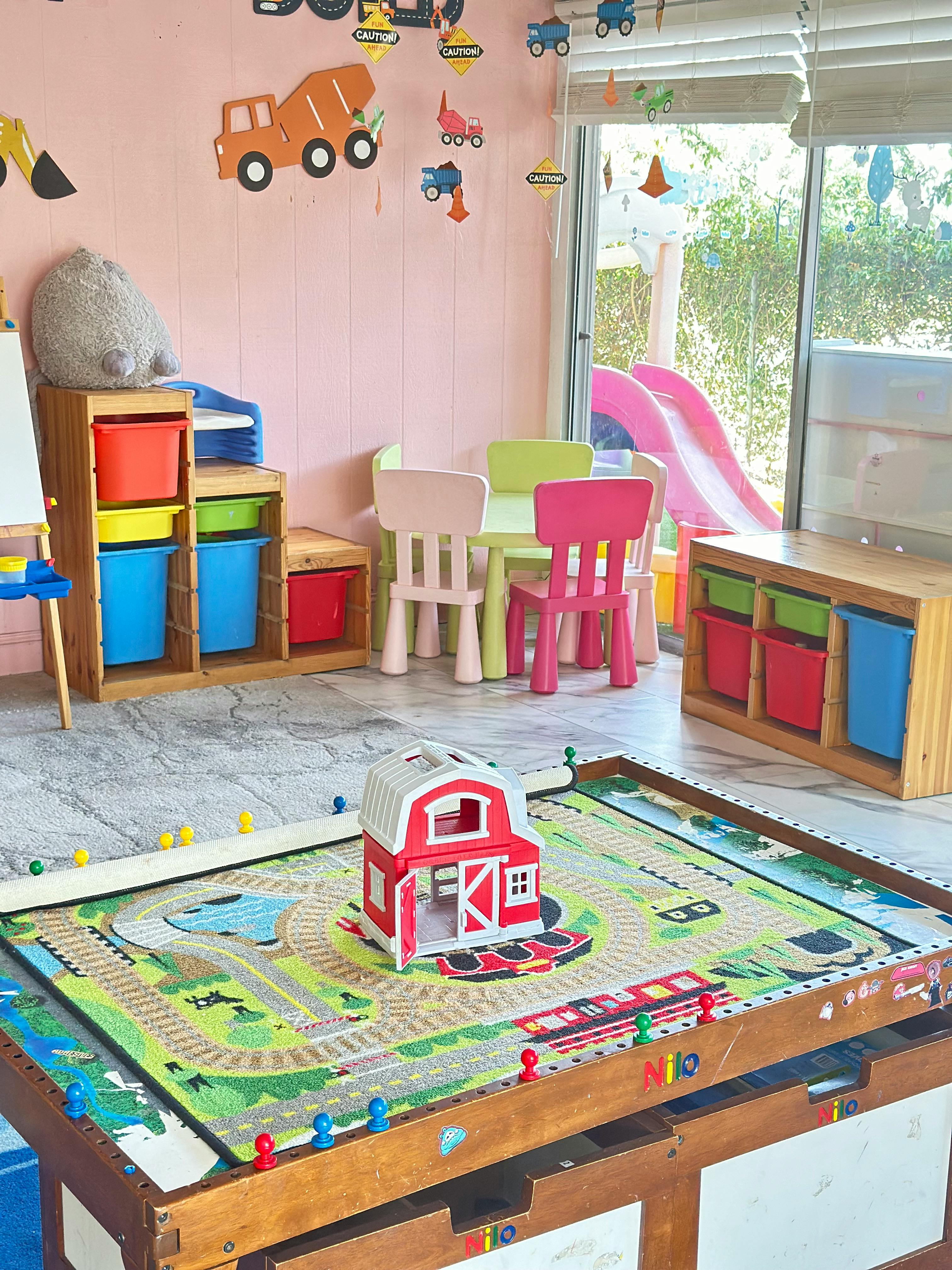 Playroom with a toy barn on a playmat, small table and chairs, and storage bins
