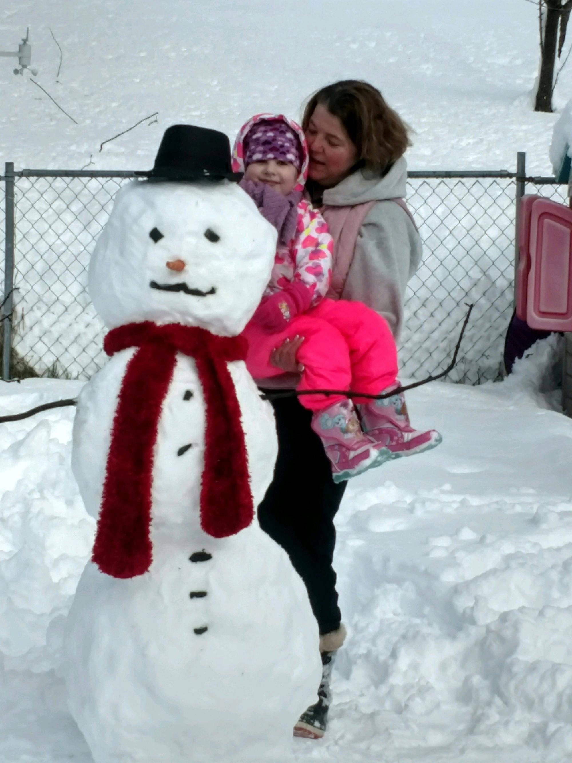 Person holding a child next to a snowman