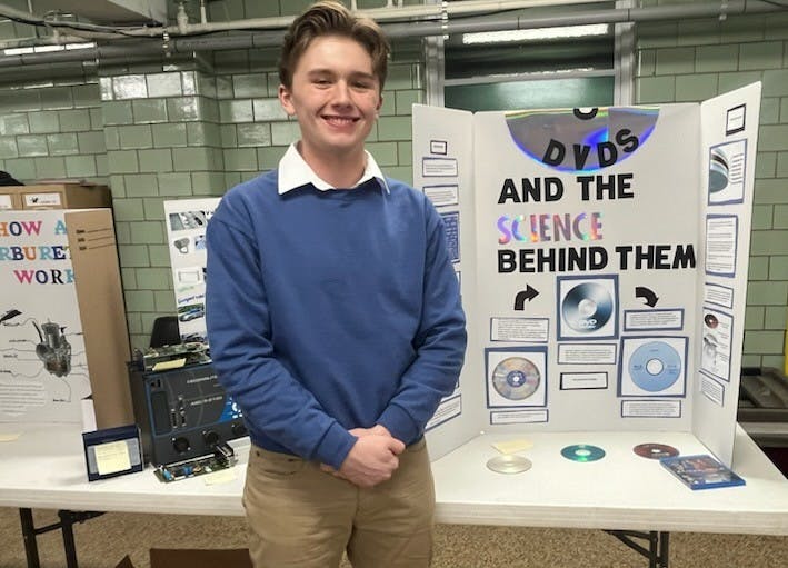 Smiling teen next to a science fair board about DVDs
