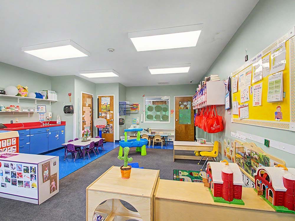 An empty daycare classroom with small tables and chairs, toys, and cabinets