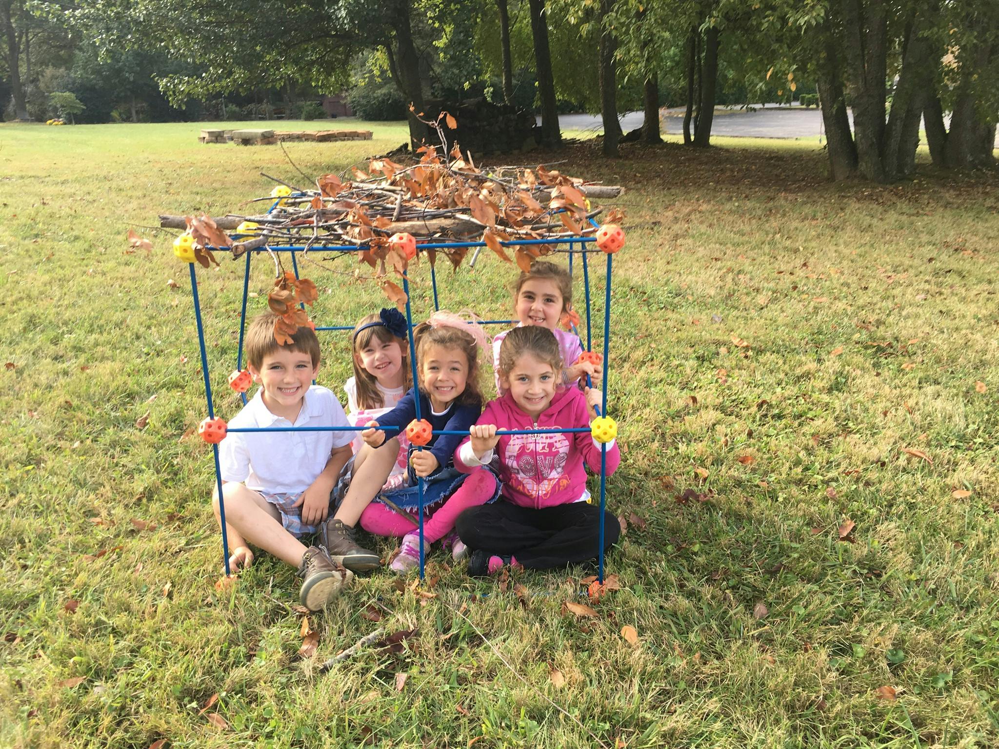 Five children sitting inside a fort made of sticks and leaves