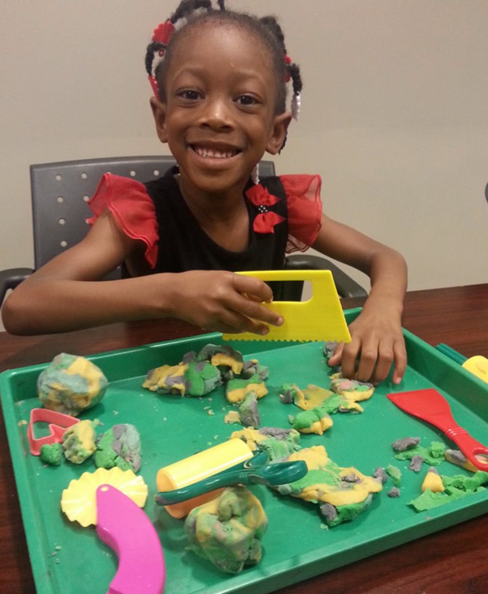 Child playing with kinetic sand and tools on a green tray