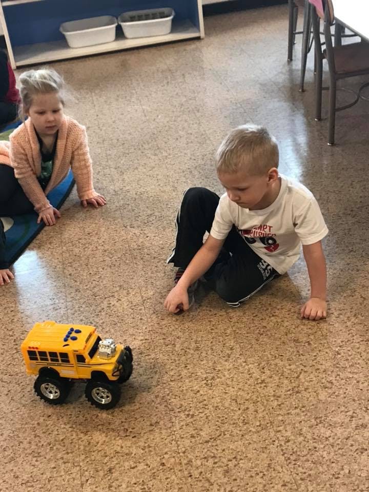 Two children playing on the floor with a toy school bus