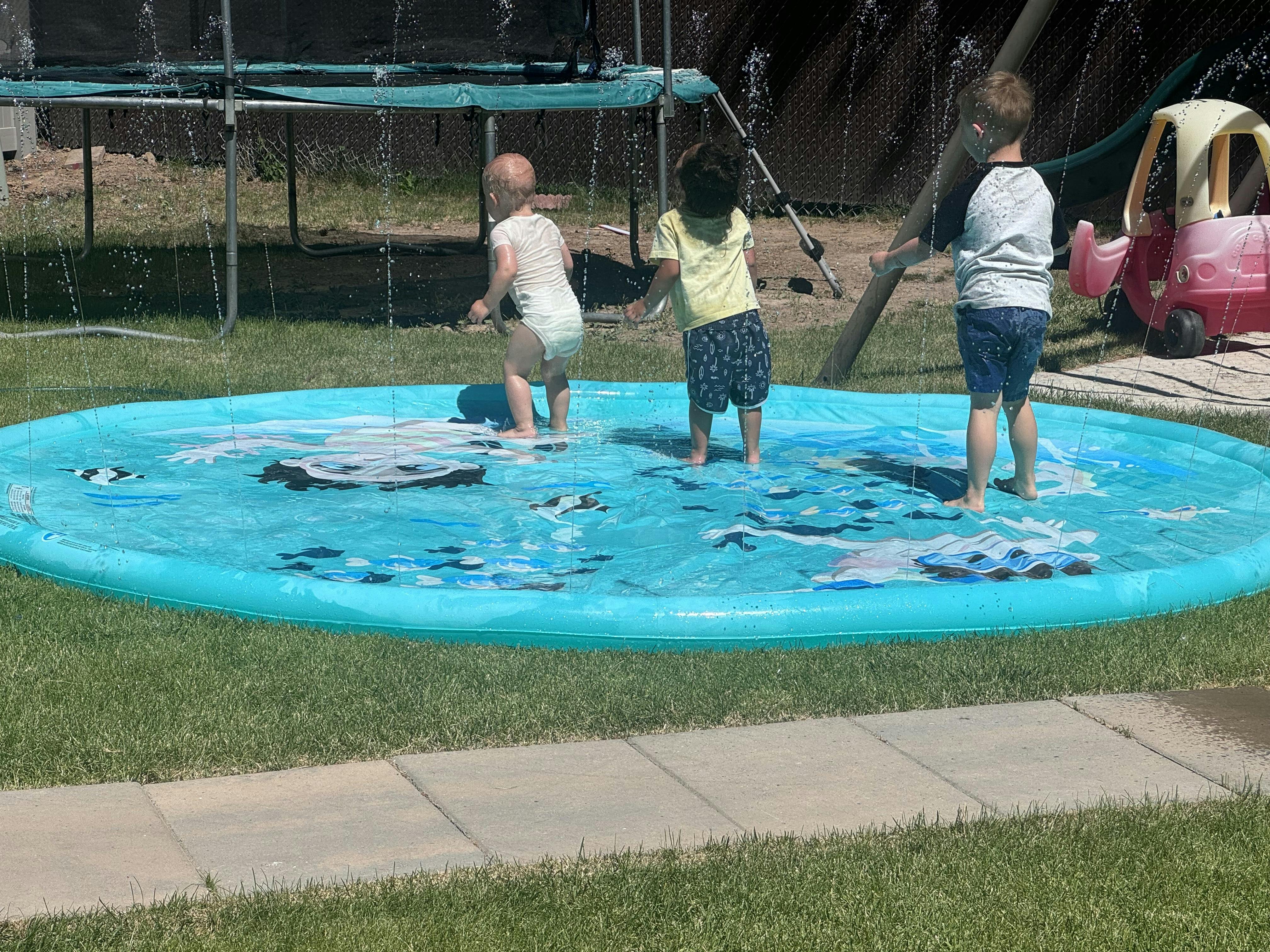 Three children playing in a shallow inflatable pool