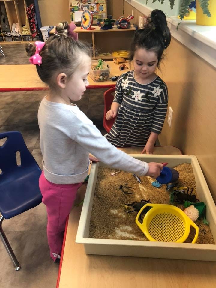 Two children playing with sand and toys in a classroom