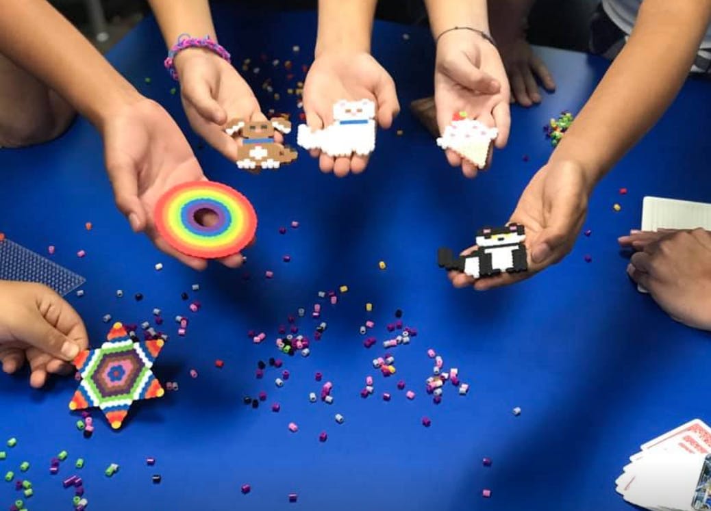 People holding colorful bead art creations over a blue table