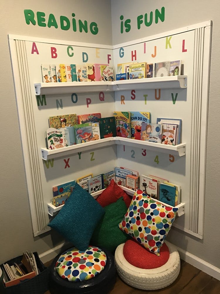 Corner reading nook with shelves of children's books, colorful pillows, and alphabet letters on the wall