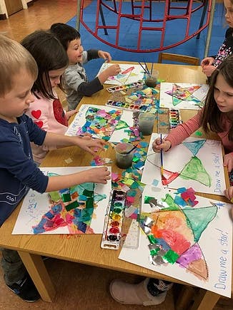 Children painting and gluing paper pieces at a table