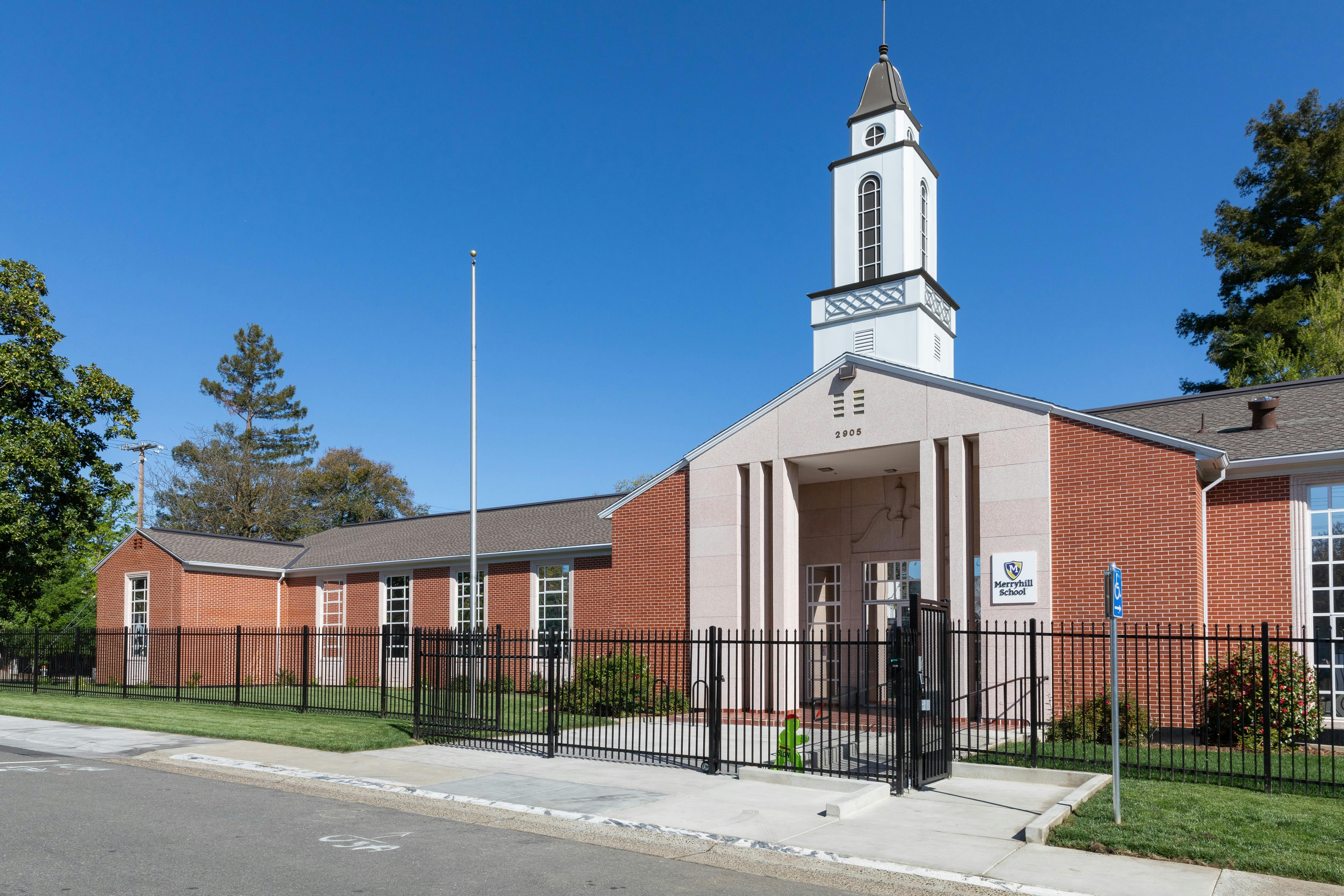 Brick building with a white steeple and a black fence