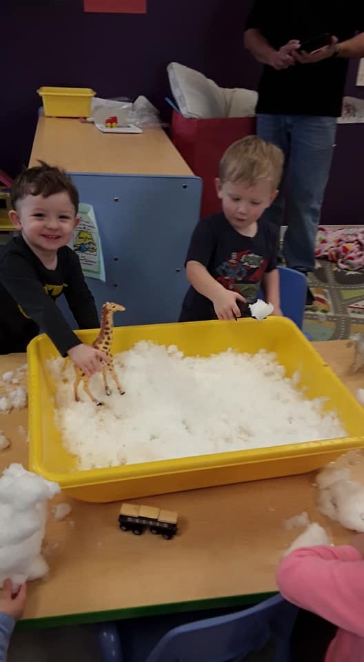 Two children playing with a giraffe toy in a bin of white fluffy material