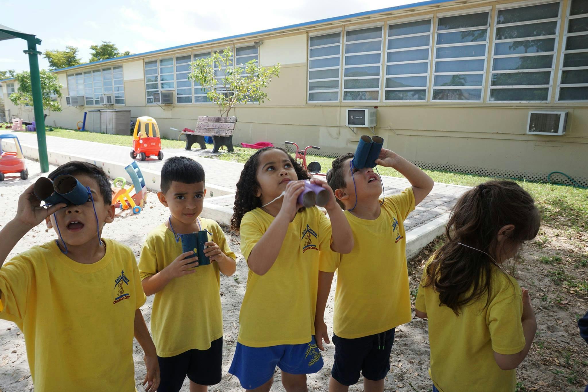 Children in yellow shirts looking up with handmade binoculars