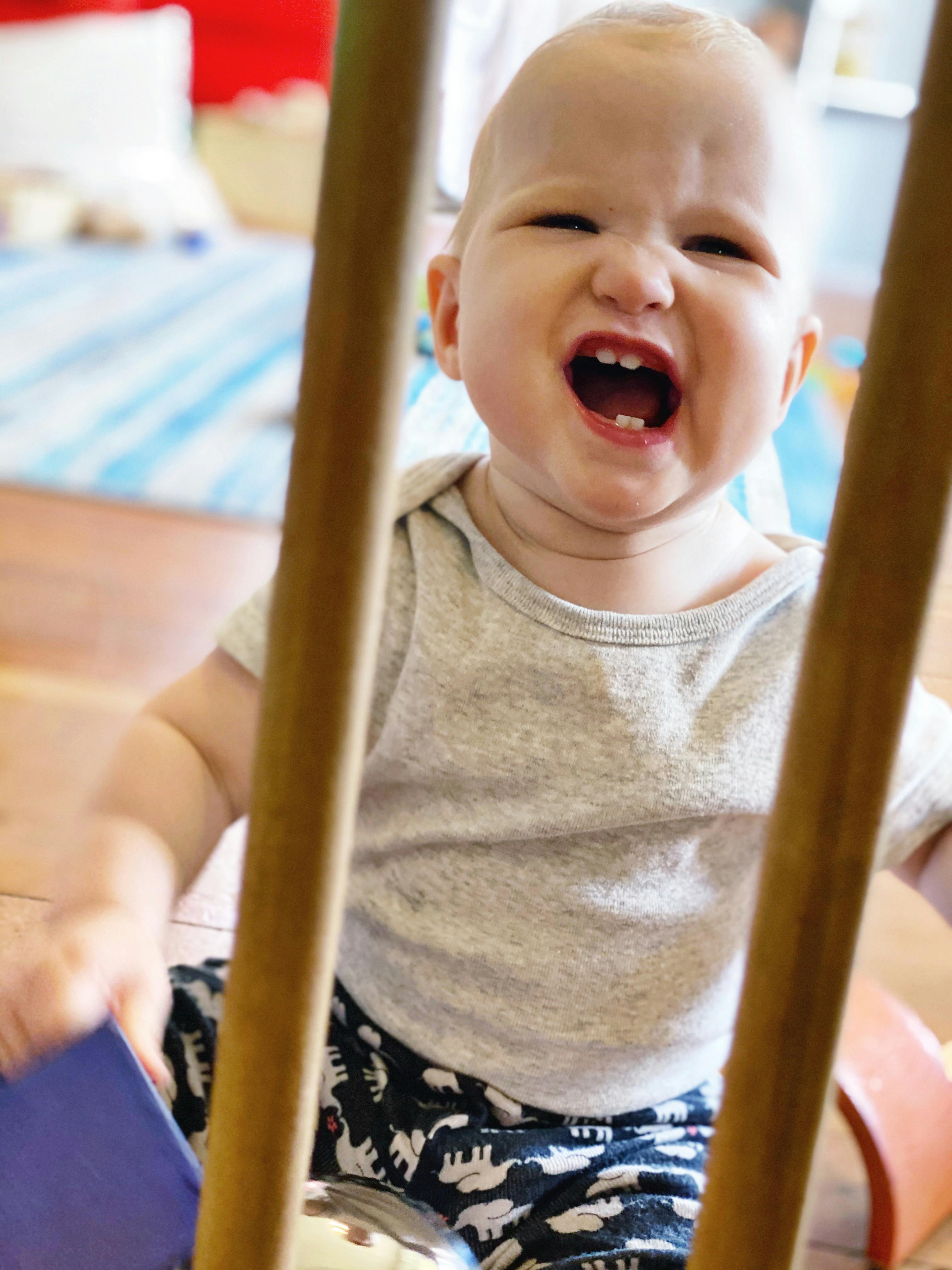 Child with mouth open, showing teeth, behind wooden bars