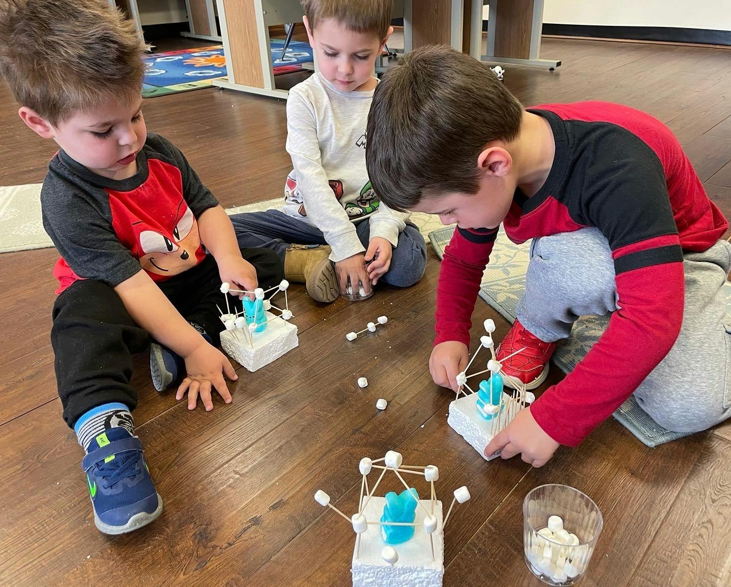 Three children building structures with marshmallows and toothpicks