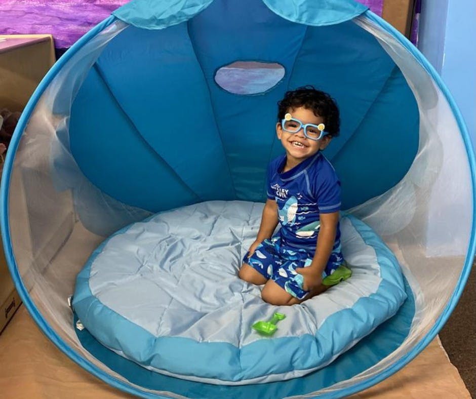 Child in blue swimwear and goggles kneeling in a blue pop-up tent