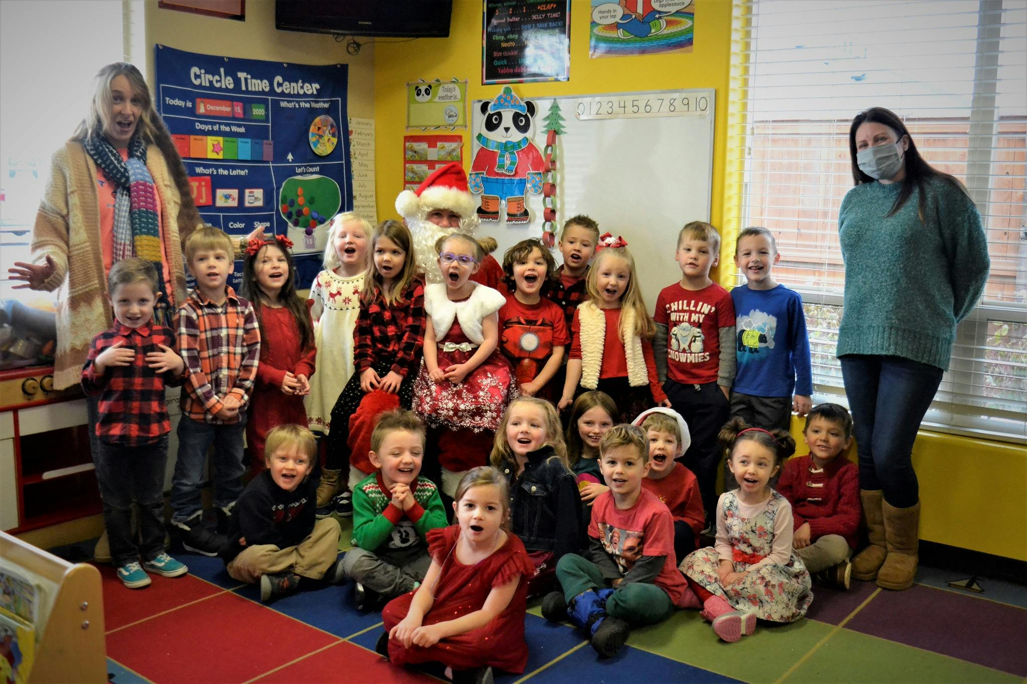 Adults and children posing with a person dressed as Santa Claus in a classroom