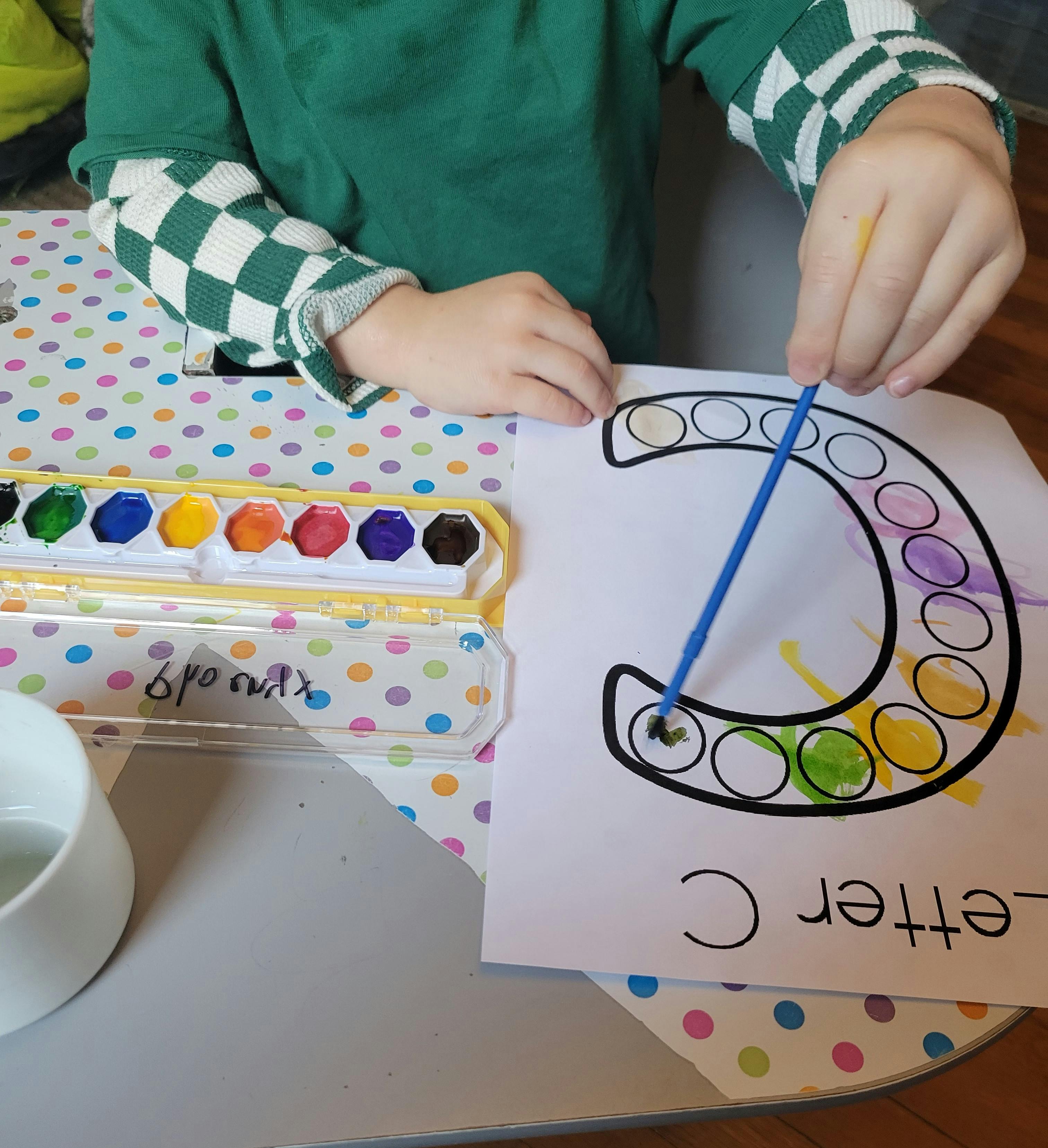 Child painting a letter C with watercolors