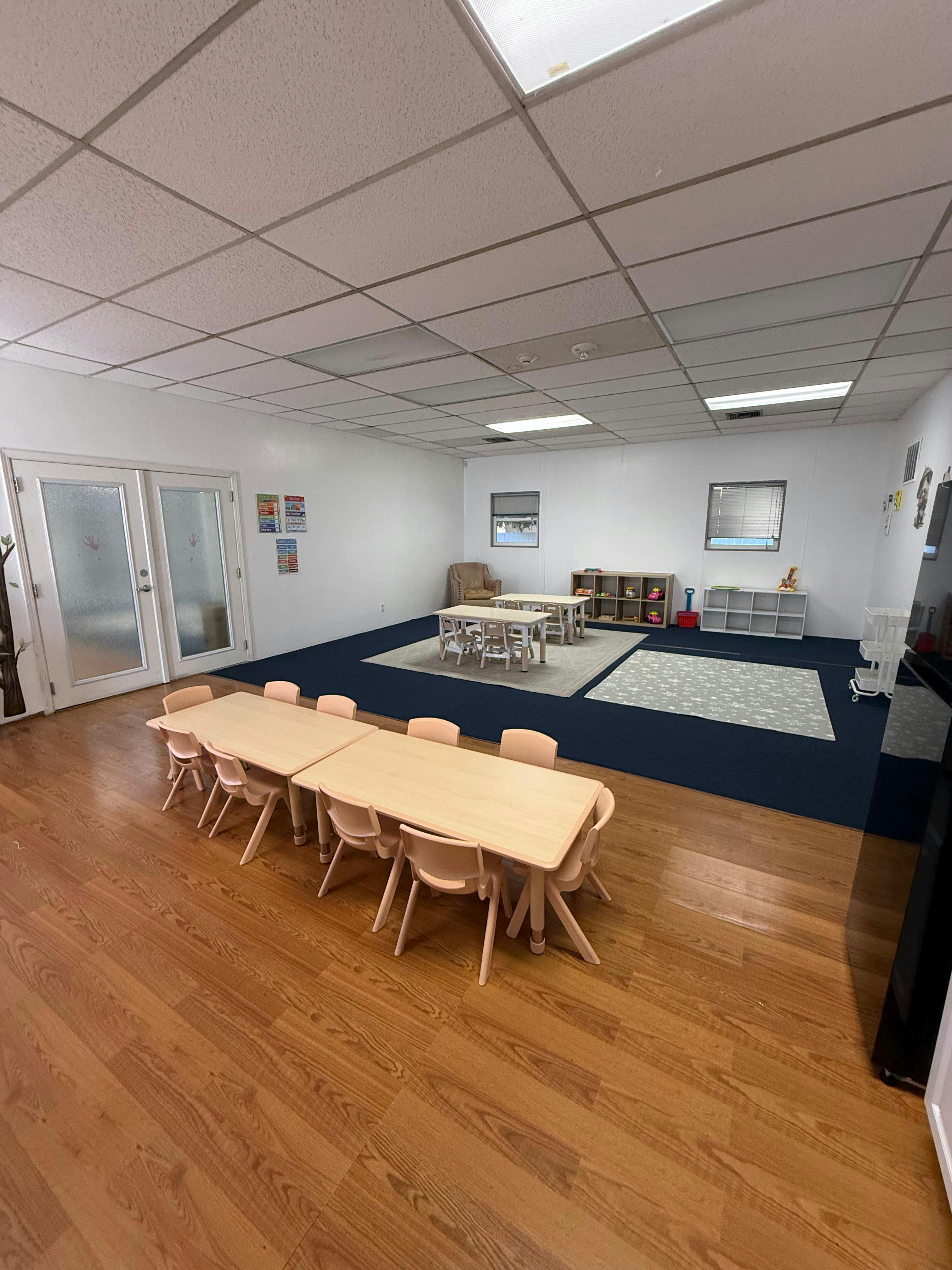 An empty childcare classroom with small tables and chairs for children