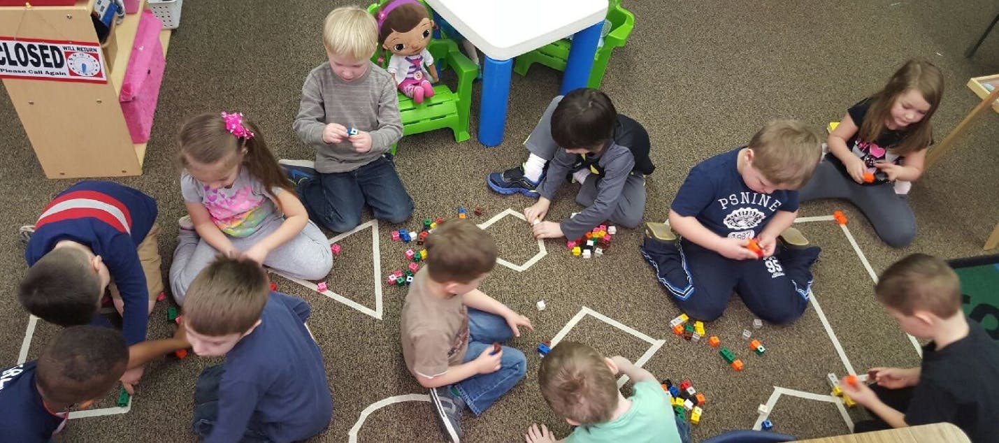 Children playing with small objects on a carpet with taped shapes