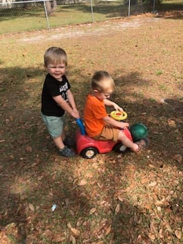 Child pushing another child in a toy car outdoors