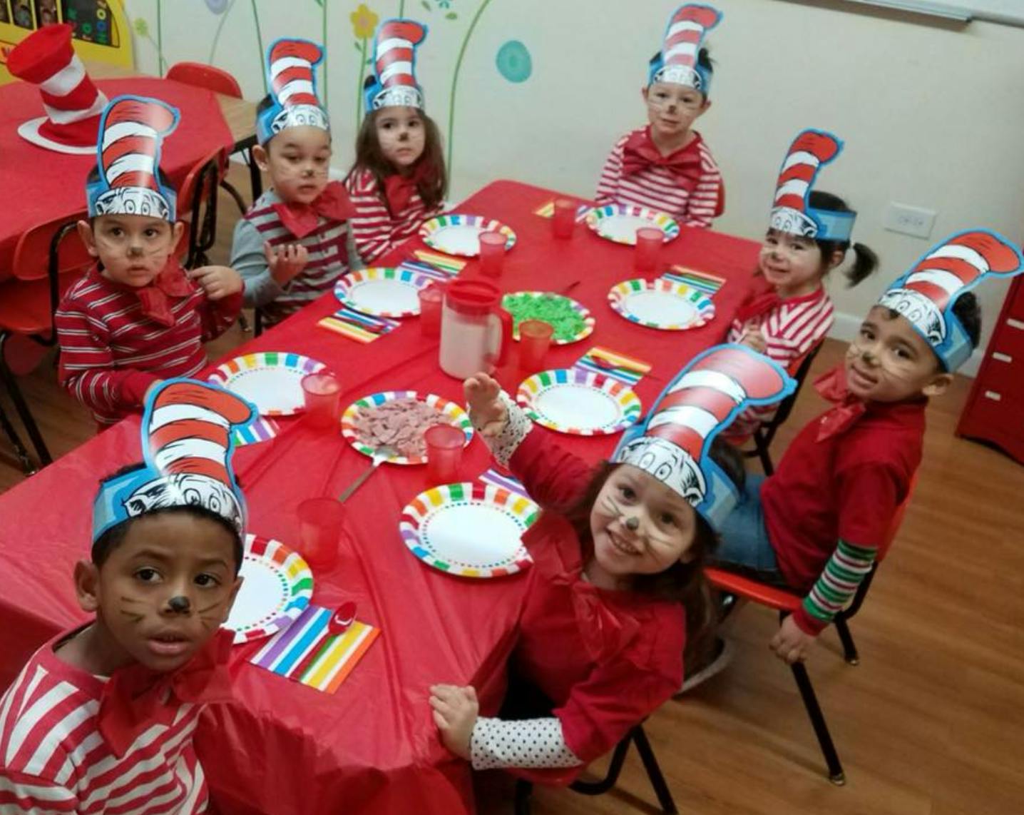 Children wearing striped hats sitting at a table with red tablecloth