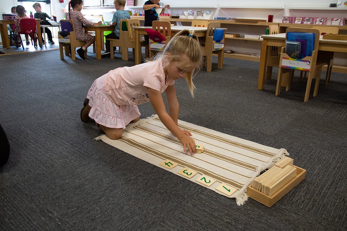 Child kneeling on floor, working with a number mat and wooden blocks in a classroom