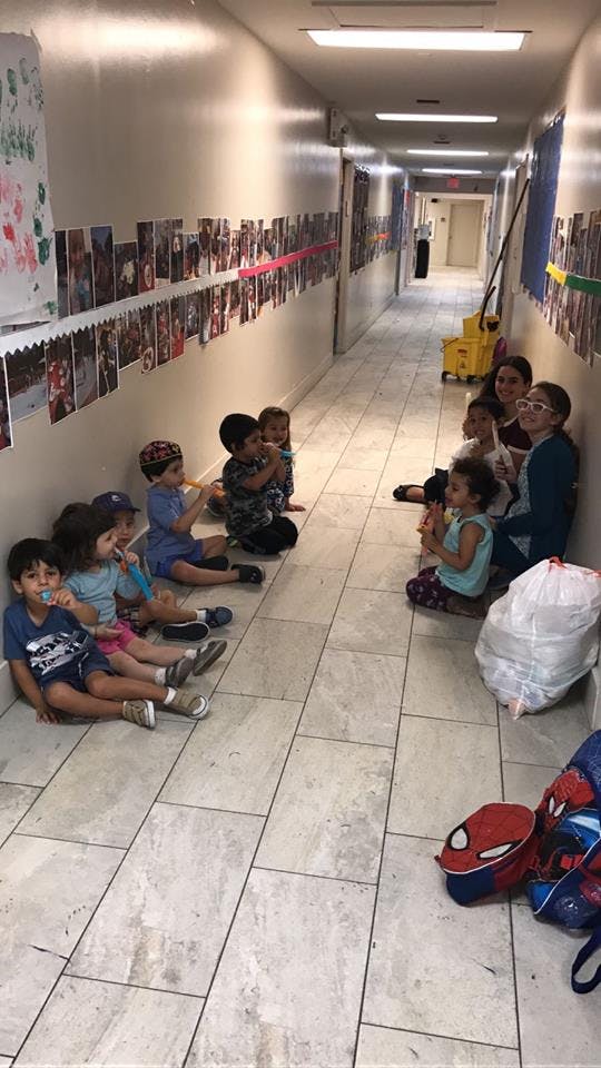 Children and adults sitting on the floor in a hallway