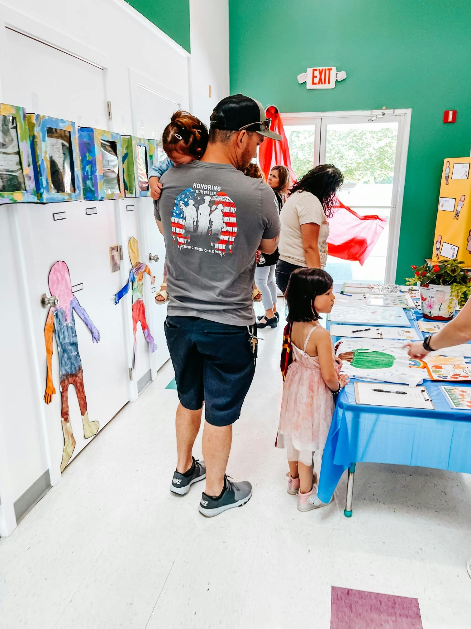Person holding a child, another child standing by a table with papers