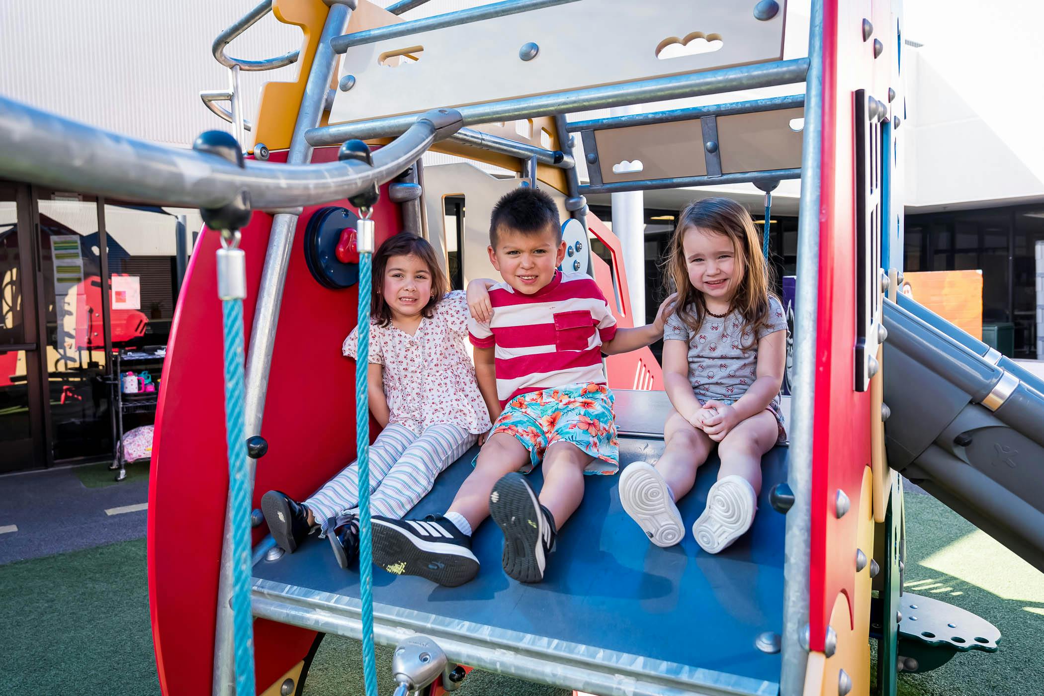 Three children sitting together on a playground structure