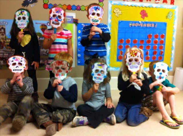 Children holding up colorful sugar skull masks in a classroom