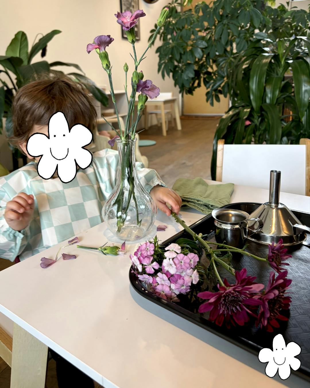Child arranging purple flowers in a clear vase on a white table