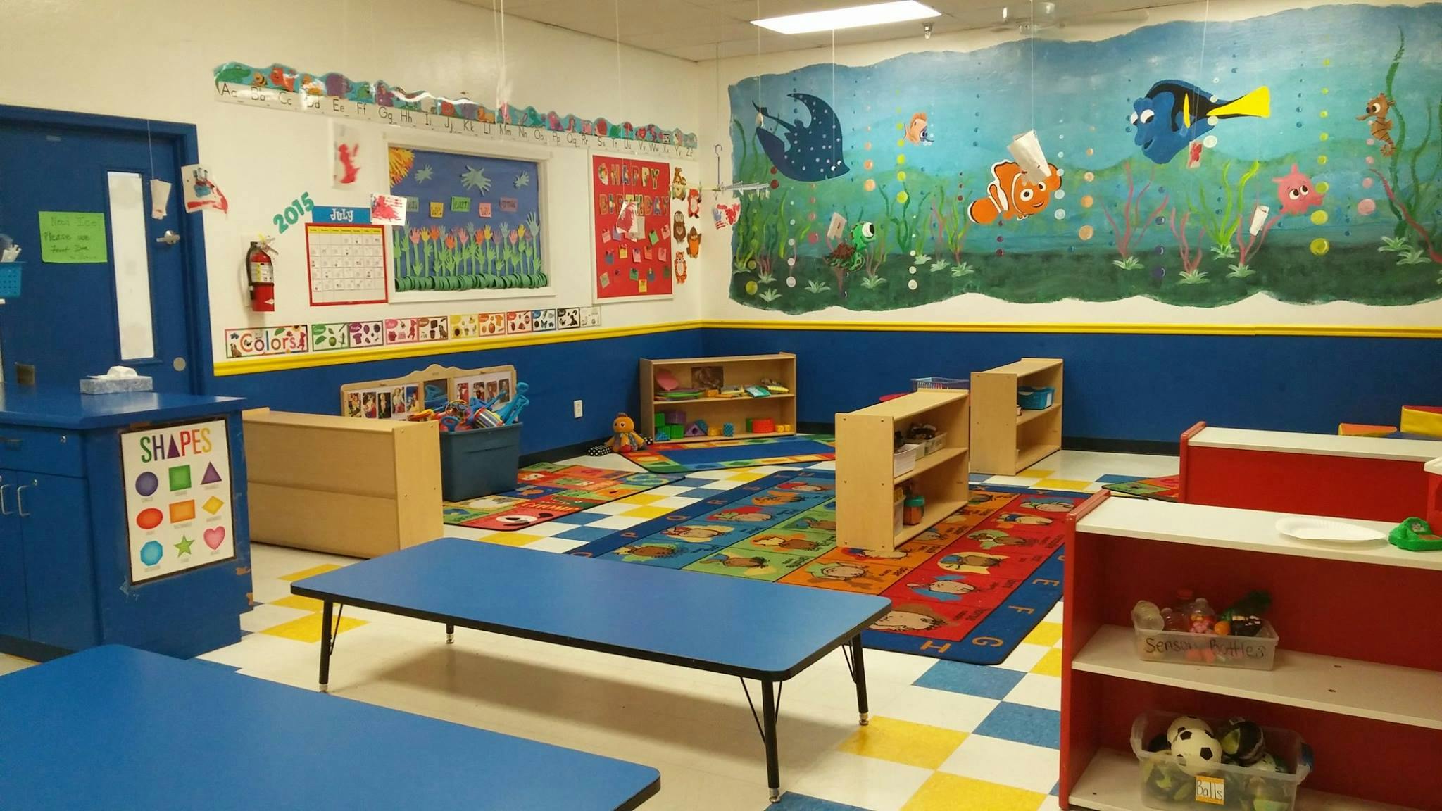 Colorful classroom with small tables and chairs, and a mural of fish