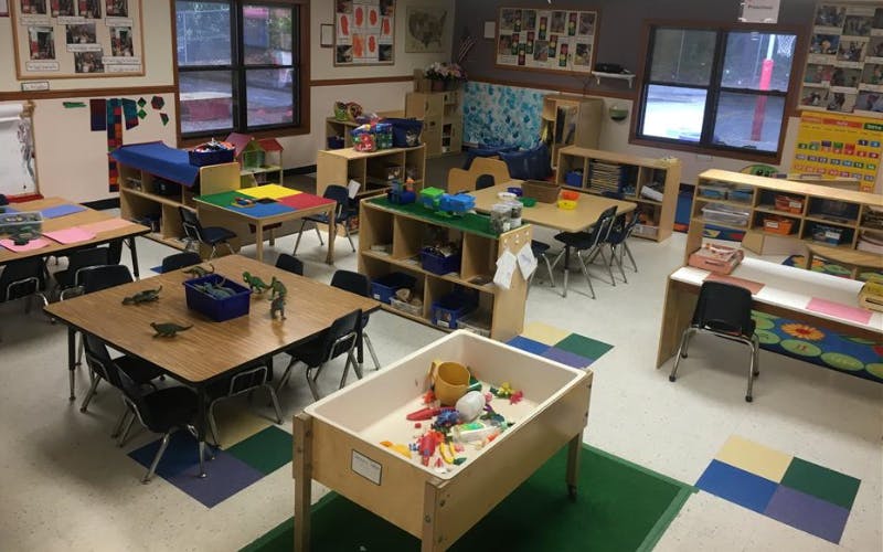 An empty preschool classroom with tables, chairs, and various play areas