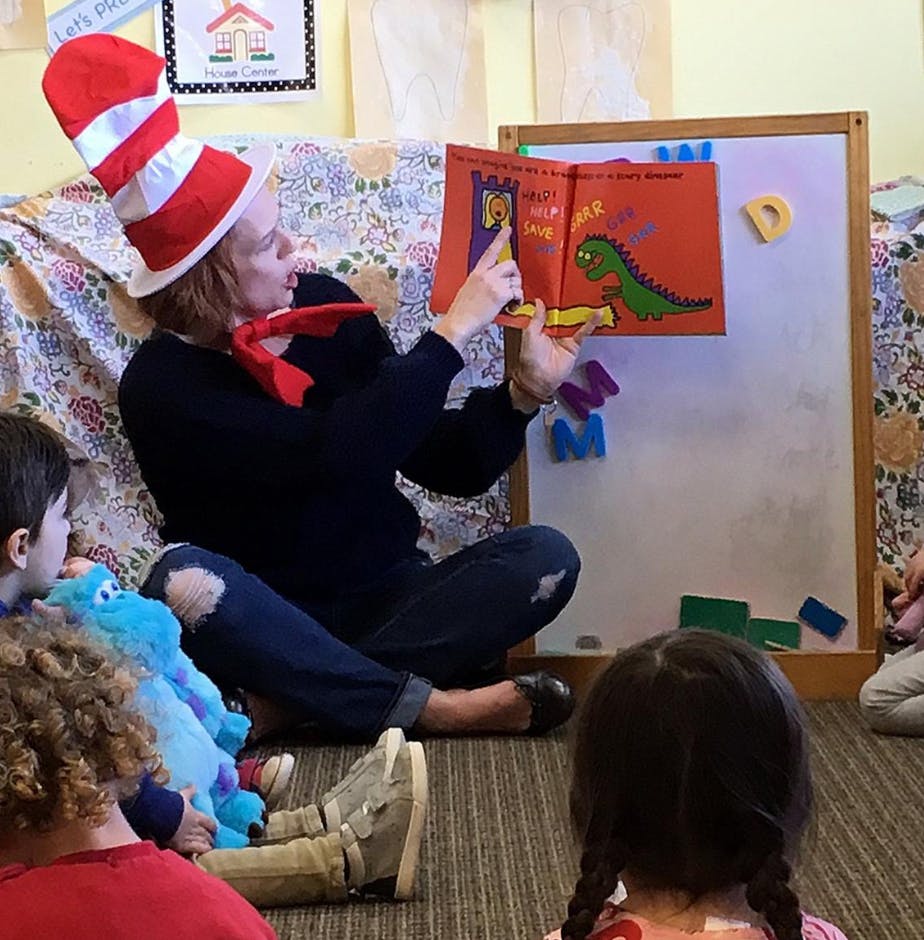 Person in striped hat reading a book to children