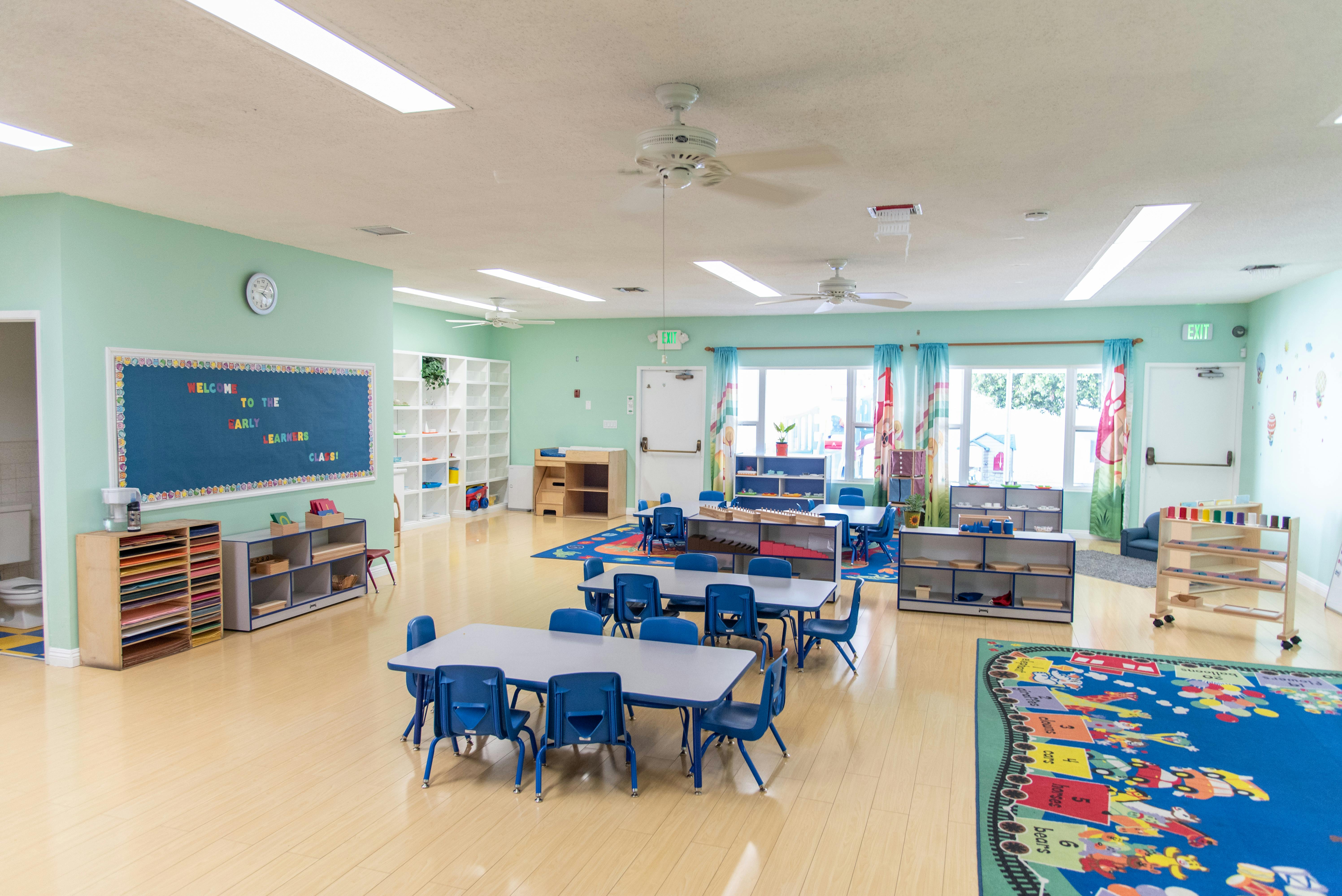 Classroom with small tables and chairs, a chalkboard, and shelves