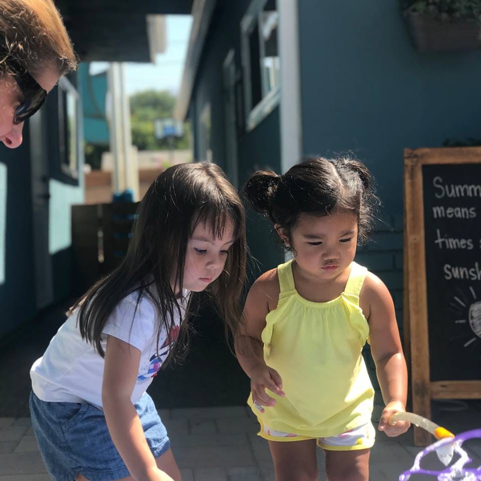 Two children looking down at something with an adult partially visible