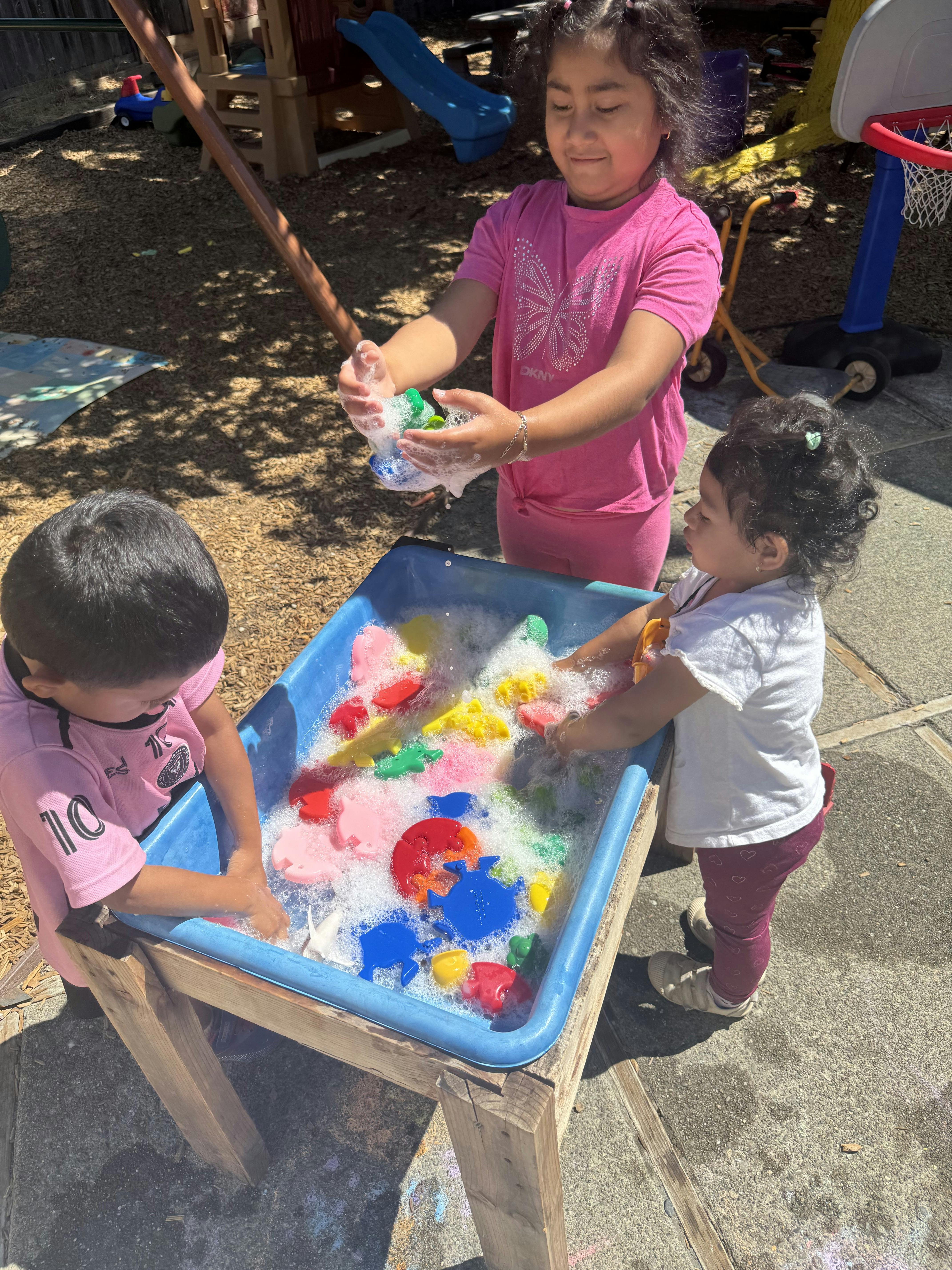 Three children playing with toys in a water table