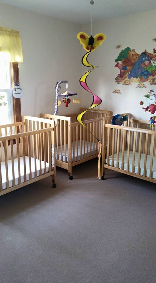 Three empty cribs in a room with a butterfly mobile