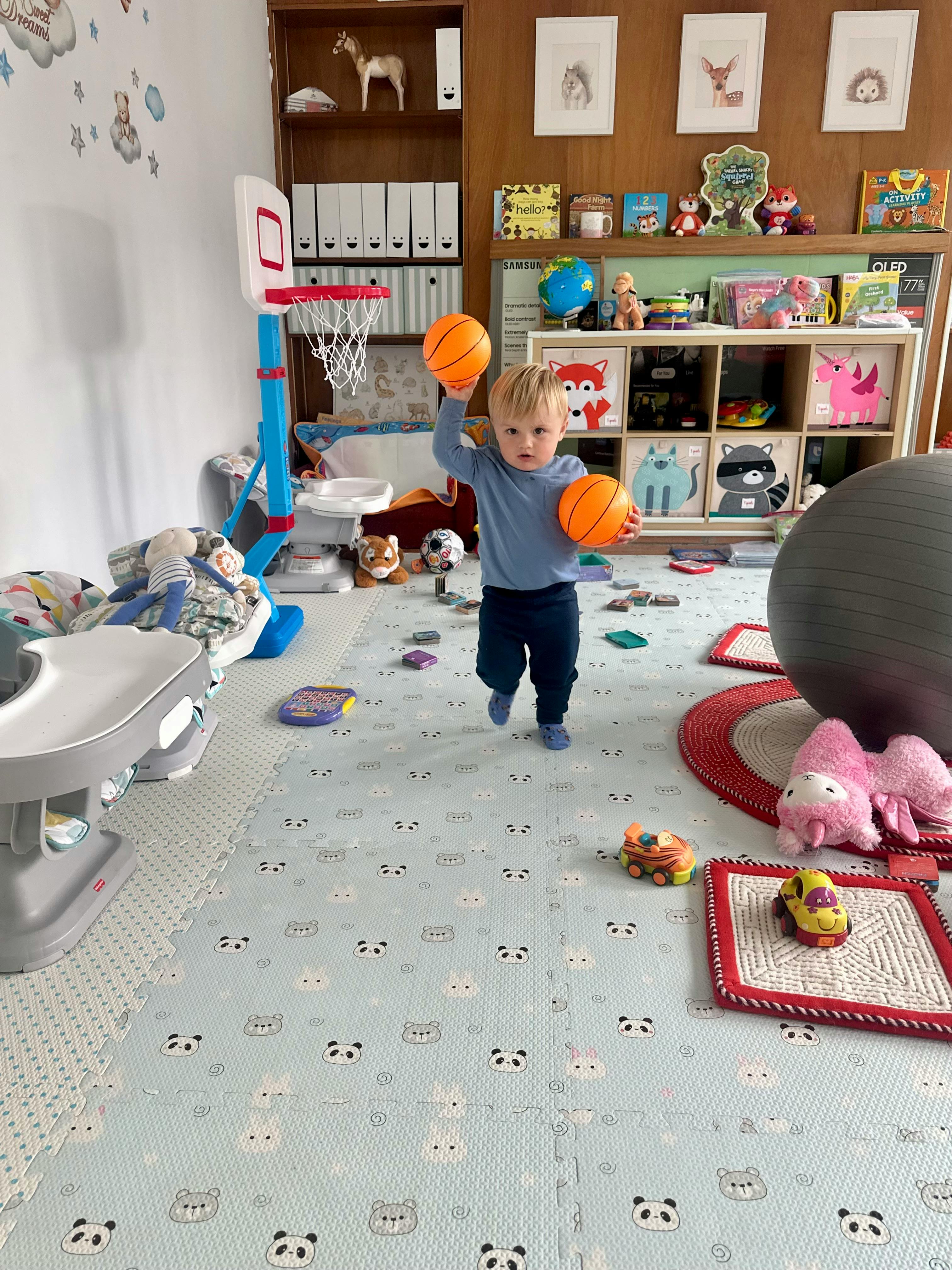 Child holding two toy basketballs in a playroom