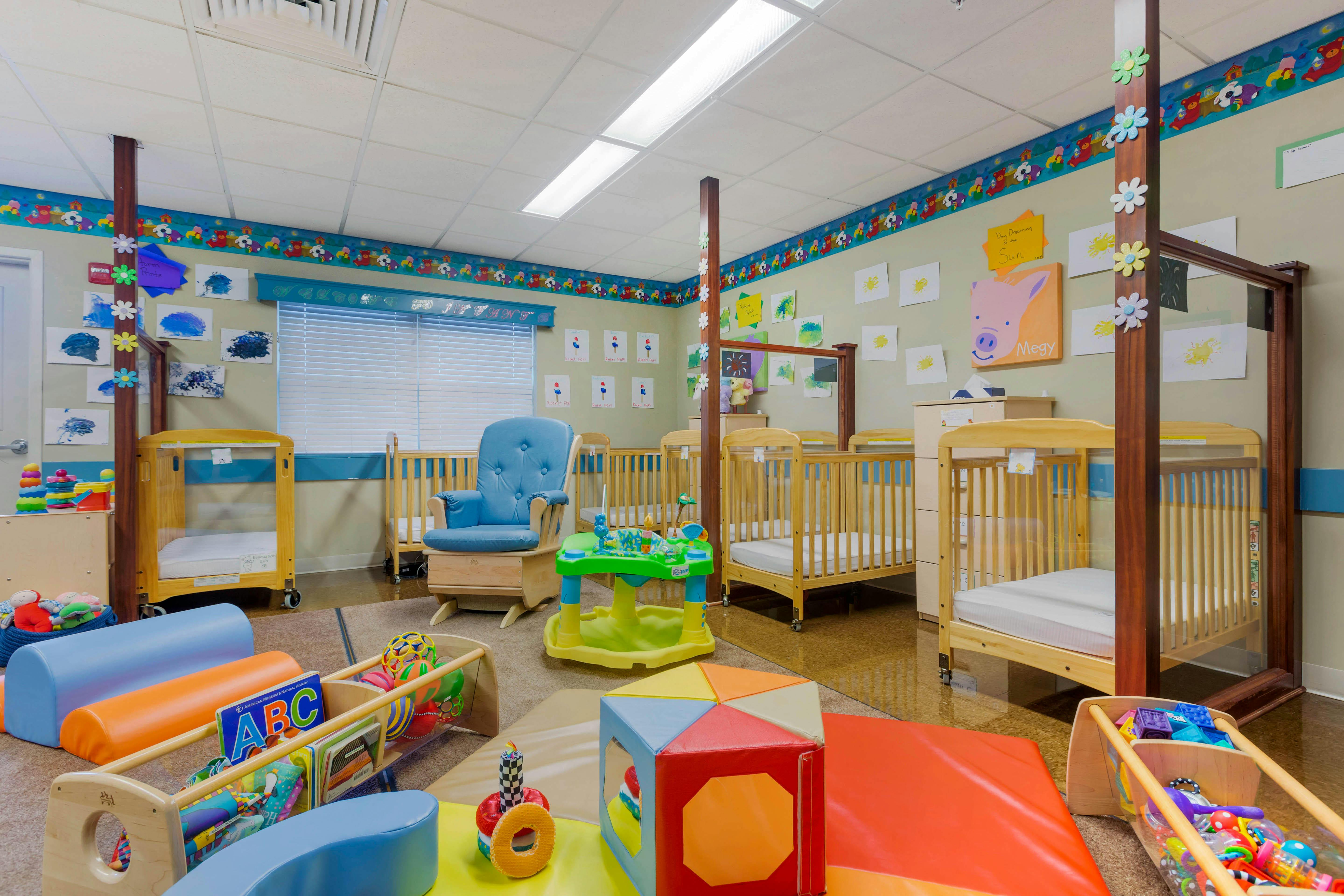Nursery room with multiple cribs, a rocking chair, and play mats with toys