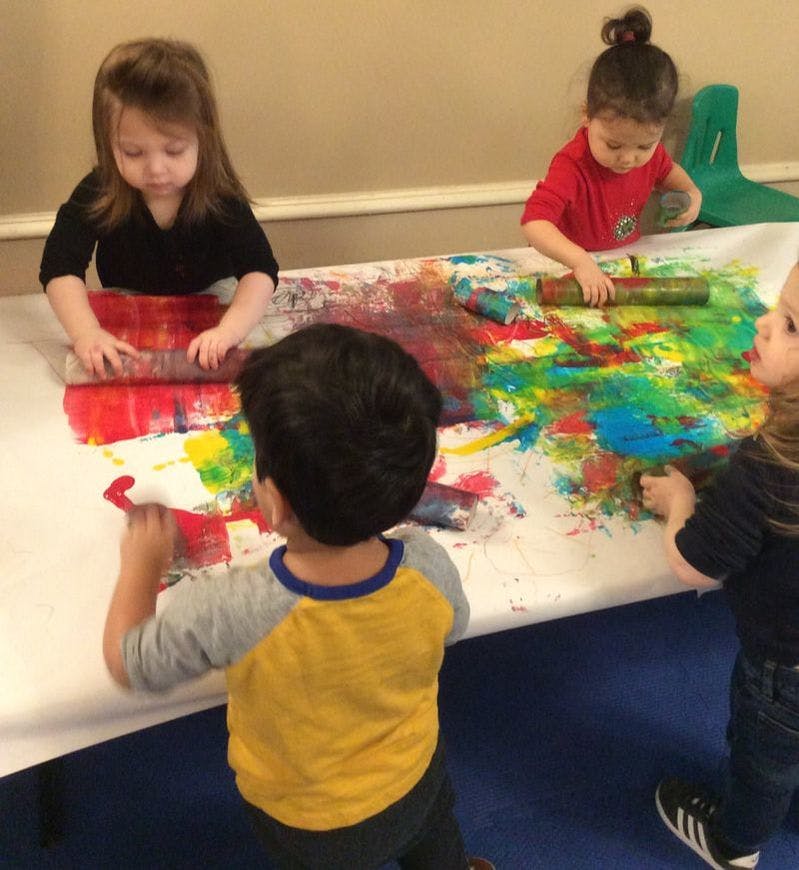 Children painting on a large sheet of paper with rollers and brushes
