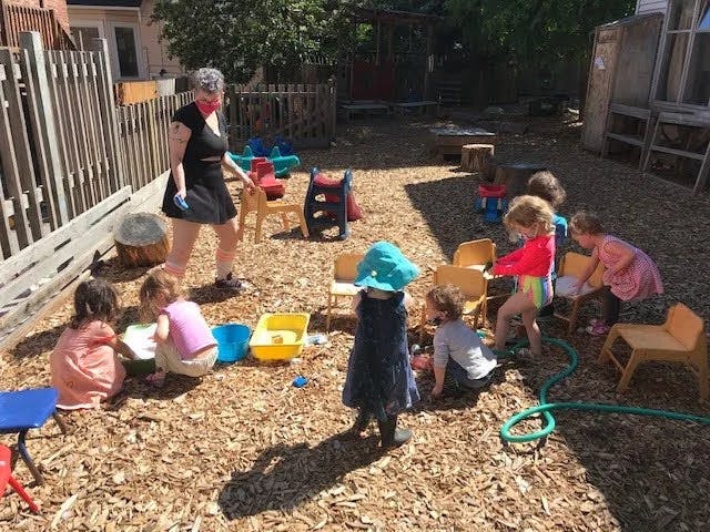 Adult and multiple children playing with water and toys outdoors